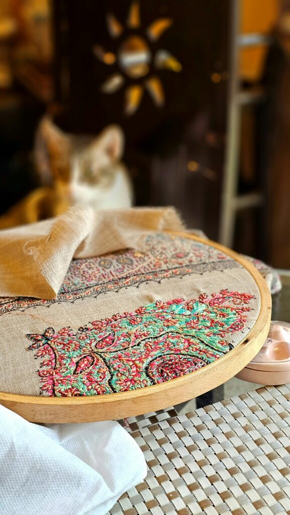 Detailed view of a vibrant embroidery hoop featuring a traditional artisan pattern with blurred cat in the background.